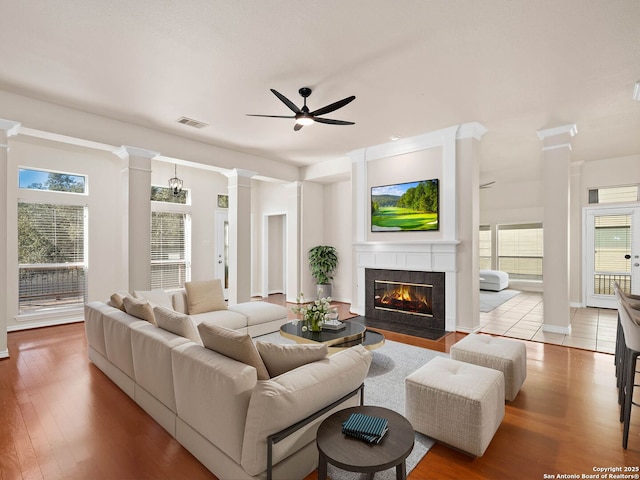 living room with ornate columns, a tiled fireplace, ceiling fan, and light wood-type flooring