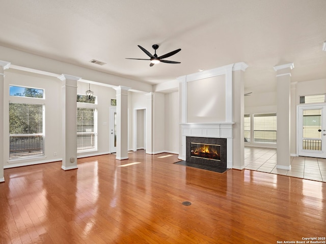 unfurnished living room featuring decorative columns, ceiling fan, a fireplace, and light wood-type flooring