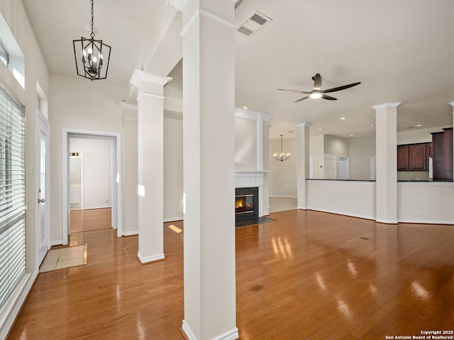 unfurnished living room featuring ceiling fan with notable chandelier, decorative columns, and light hardwood / wood-style floors