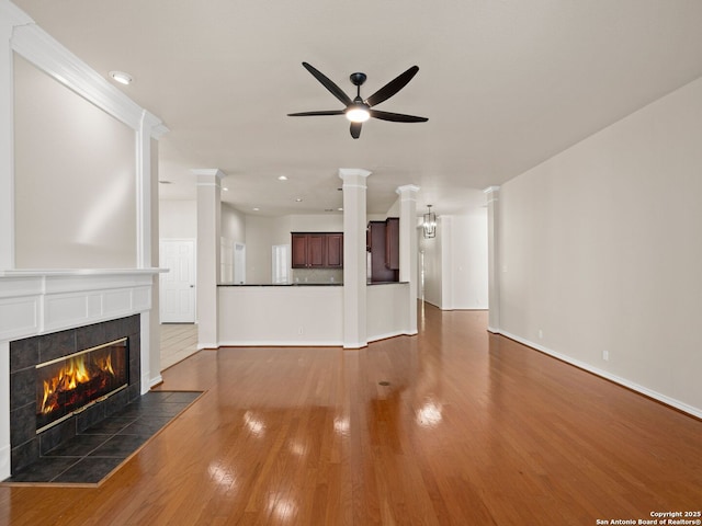 unfurnished living room with ceiling fan, dark hardwood / wood-style flooring, a tiled fireplace, and ornate columns