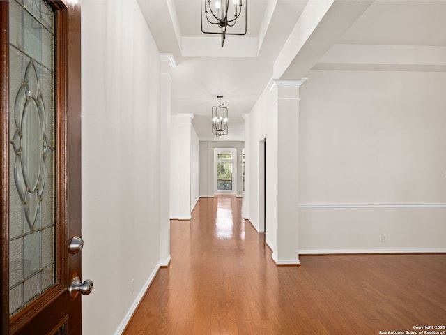 hall featuring ornate columns, hardwood / wood-style floors, a chandelier, and a tray ceiling