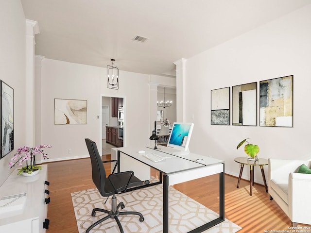 office with ornate columns, an inviting chandelier, and light hardwood / wood-style flooring