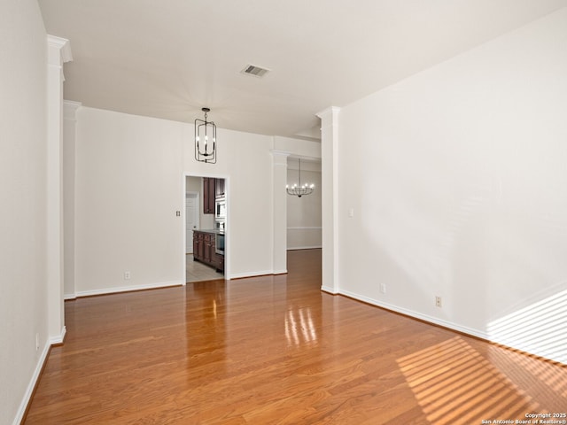 spare room with ornate columns, hardwood / wood-style floors, and an inviting chandelier