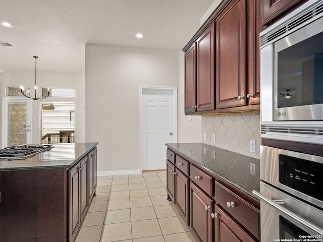 kitchen featuring light tile patterned flooring, dark stone counters, hanging light fixtures, decorative backsplash, and stainless steel appliances