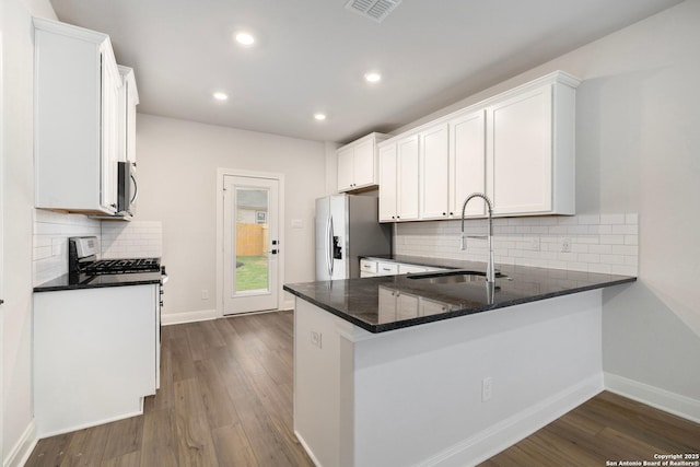 kitchen with sink, appliances with stainless steel finishes, white cabinetry, dark hardwood / wood-style flooring, and kitchen peninsula