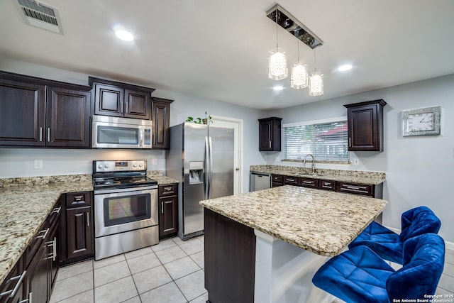 kitchen featuring a kitchen bar, sink, dark brown cabinets, appliances with stainless steel finishes, and a kitchen island