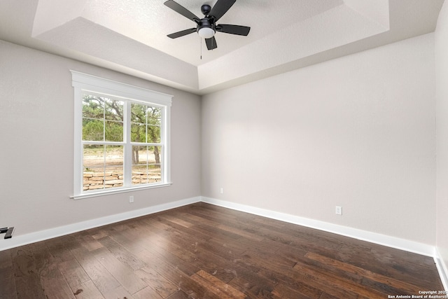 empty room featuring a raised ceiling, dark hardwood / wood-style floors, and ceiling fan