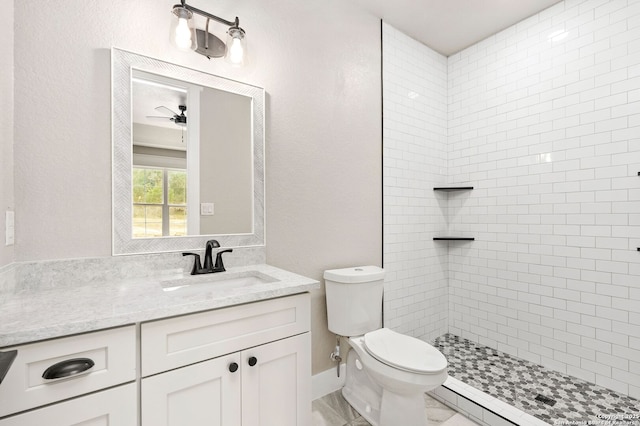 bathroom with ceiling fan, baseboard heating, vanity, a tile shower, and toilet