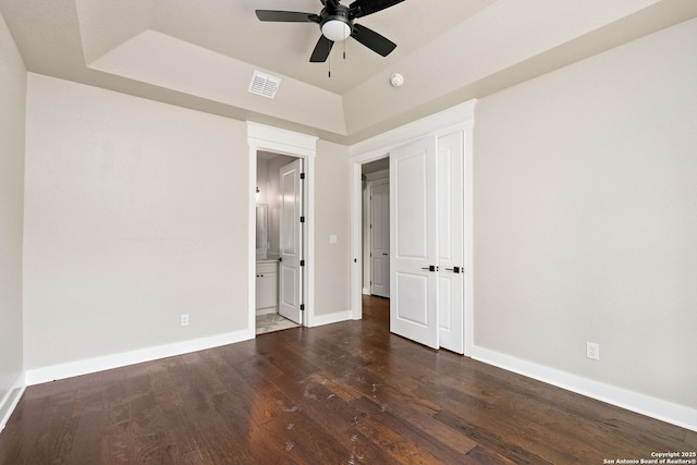 unfurnished bedroom with dark wood-type flooring, ceiling fan, connected bathroom, and a raised ceiling