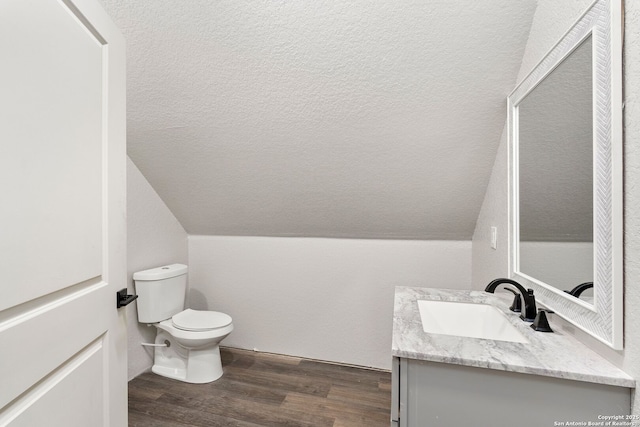 bathroom featuring vaulted ceiling, hardwood / wood-style flooring, vanity, toilet, and a textured ceiling