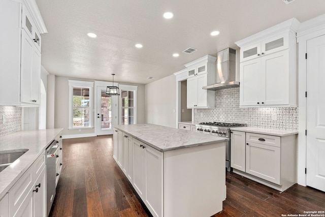 kitchen featuring white cabinetry, hanging light fixtures, a center island, stainless steel appliances, and wall chimney exhaust hood