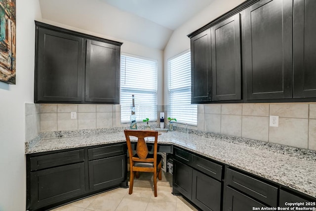 kitchen with tasteful backsplash, lofted ceiling, built in desk, and light tile patterned flooring