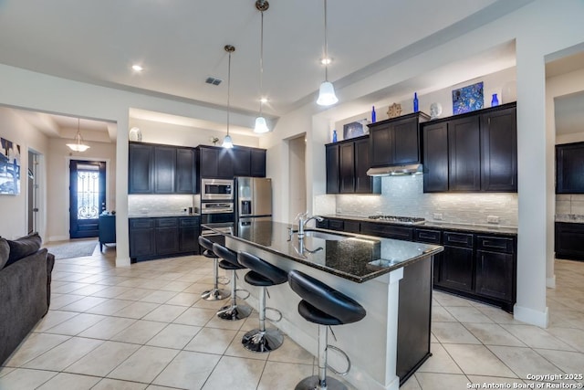 kitchen featuring light tile patterned flooring, appliances with stainless steel finishes, a kitchen island with sink, and pendant lighting