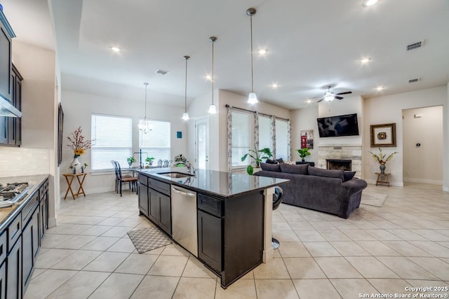 kitchen featuring pendant lighting, light tile patterned floors, stainless steel appliances, a center island with sink, and dark stone counters