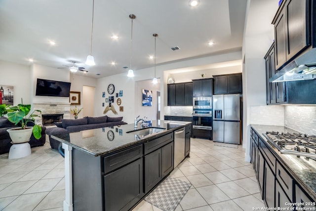 kitchen featuring sink, dark stone countertops, pendant lighting, stainless steel appliances, and a kitchen island with sink