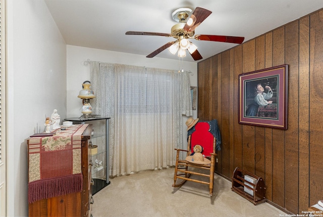 sitting room featuring light carpet, ceiling fan, and wood walls