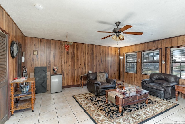 living room with ceiling fan, wood walls, a textured ceiling, and light tile patterned floors