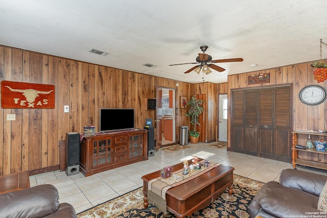 living room with wooden walls, light tile patterned floors, a textured ceiling, and ceiling fan