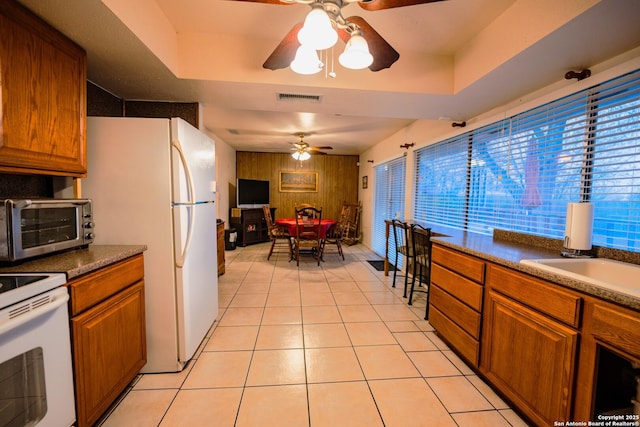 kitchen with ceiling fan, white appliances, a tray ceiling, and light tile patterned flooring