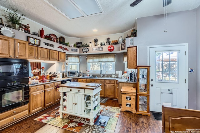 kitchen with dark wood-type flooring, a healthy amount of sunlight, a kitchen island, and black appliances