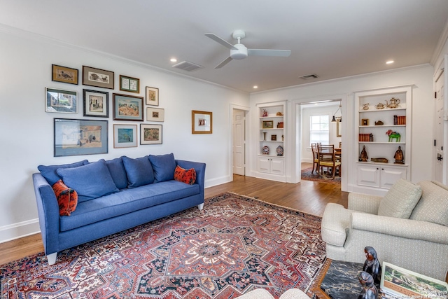 living room with built in features, crown molding, visible vents, and wood finished floors