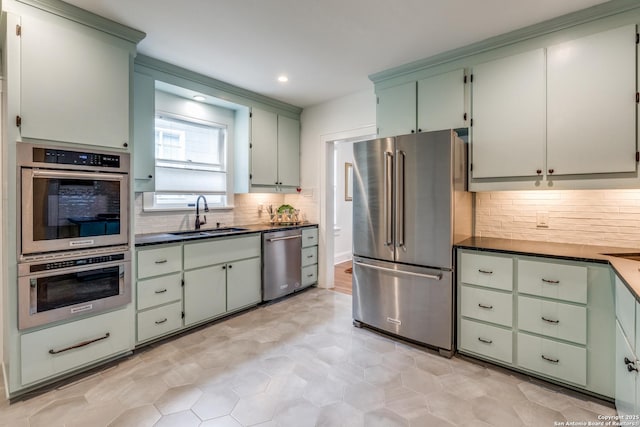 kitchen featuring tasteful backsplash, dark countertops, stainless steel appliances, green cabinets, and a sink