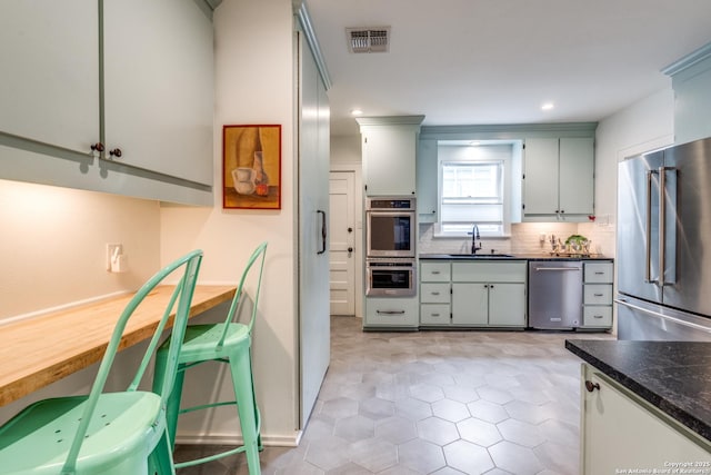 kitchen with visible vents, decorative backsplash, dark countertops, appliances with stainless steel finishes, and a sink