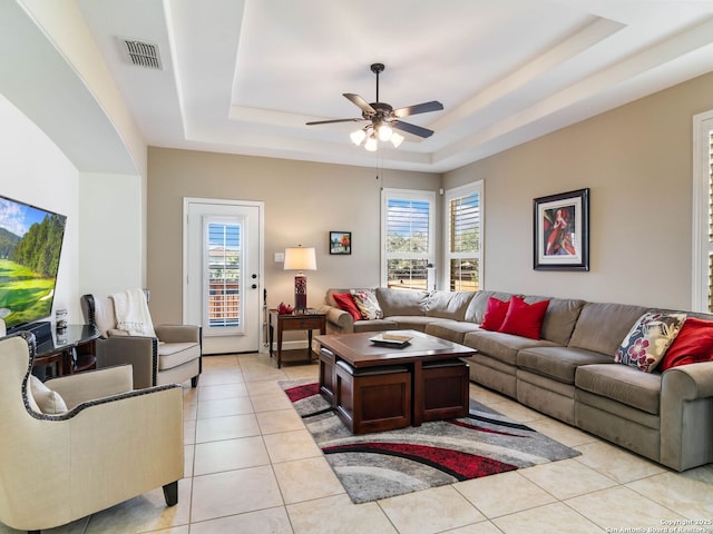 tiled living room with a raised ceiling, a wealth of natural light, and ceiling fan