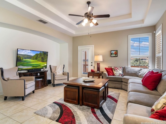 tiled living room with ceiling fan and a raised ceiling