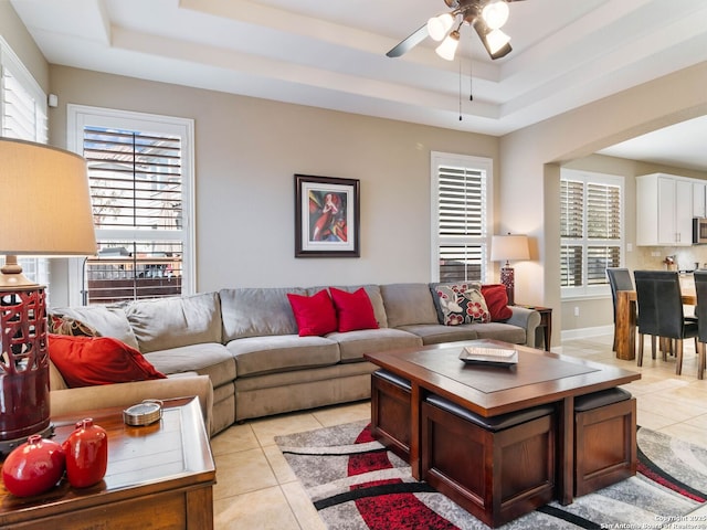 living room with light tile patterned flooring, ceiling fan, and a tray ceiling