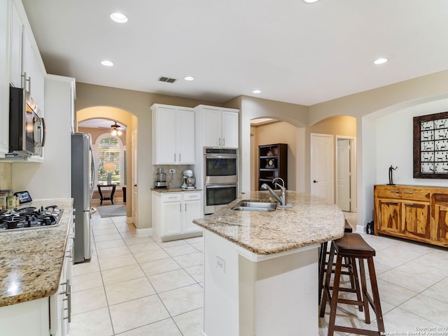 kitchen featuring appliances with stainless steel finishes, sink, white cabinets, light stone counters, and a center island with sink