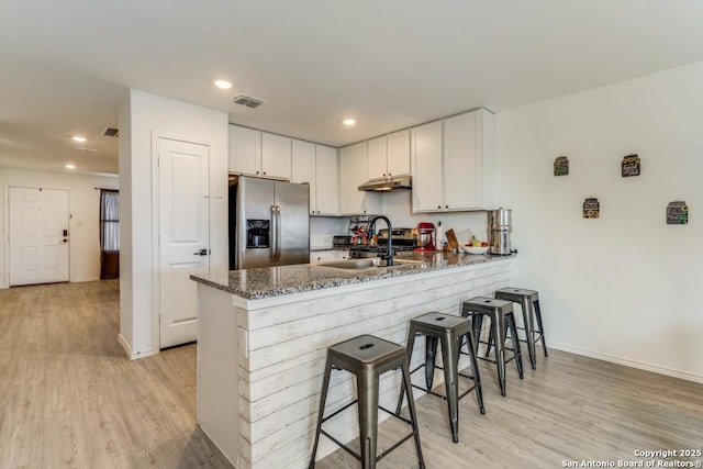 kitchen featuring stainless steel fridge, a breakfast bar, white cabinets, kitchen peninsula, and dark stone counters