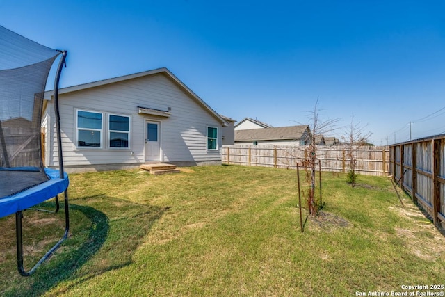 rear view of property featuring a trampoline and a lawn