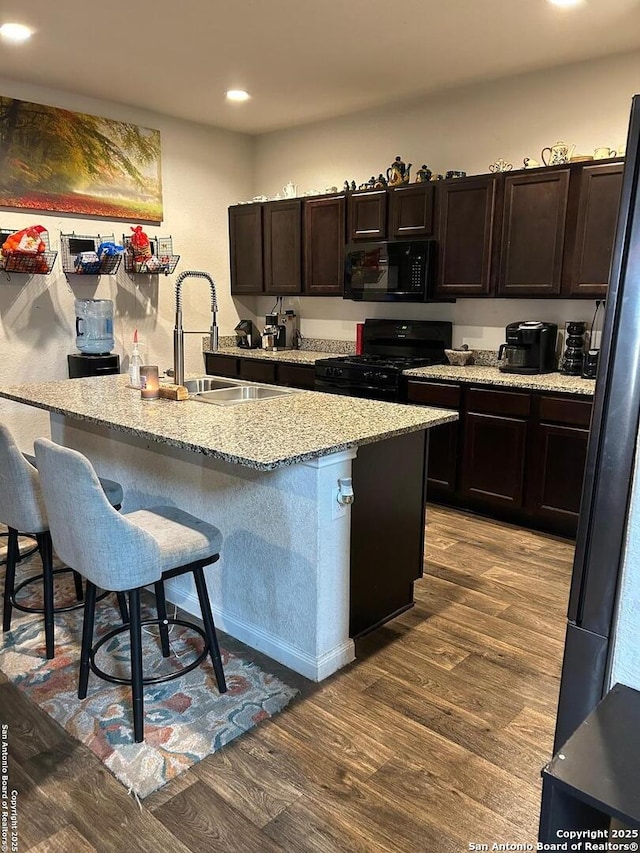 kitchen with sink, a breakfast bar, a kitchen island with sink, hardwood / wood-style floors, and black appliances