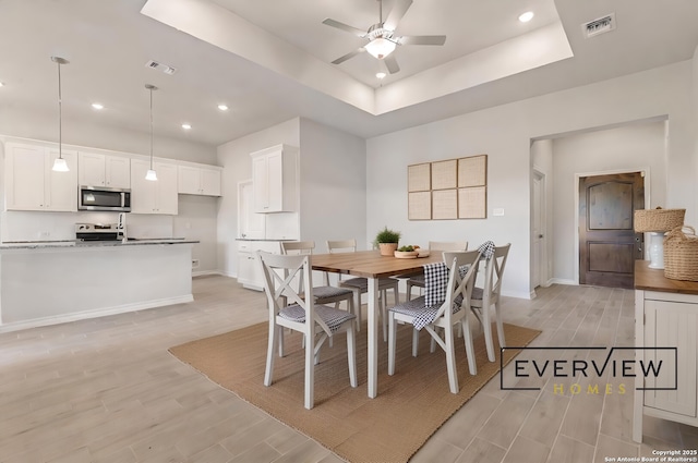 dining area featuring ceiling fan, a tray ceiling, and light hardwood / wood-style floors