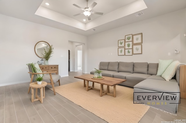 living room with a raised ceiling, wood-type flooring, and ceiling fan