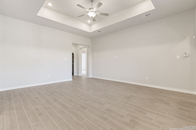 spare room featuring ceiling fan, a raised ceiling, and light wood-type flooring