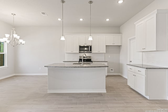 kitchen with stainless steel appliances, white cabinetry, a center island with sink, and dark stone countertops