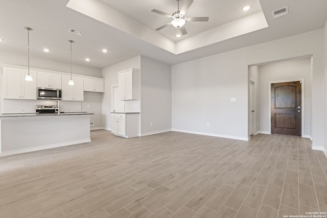 unfurnished living room featuring ceiling fan, sink, a tray ceiling, and light hardwood / wood-style floors