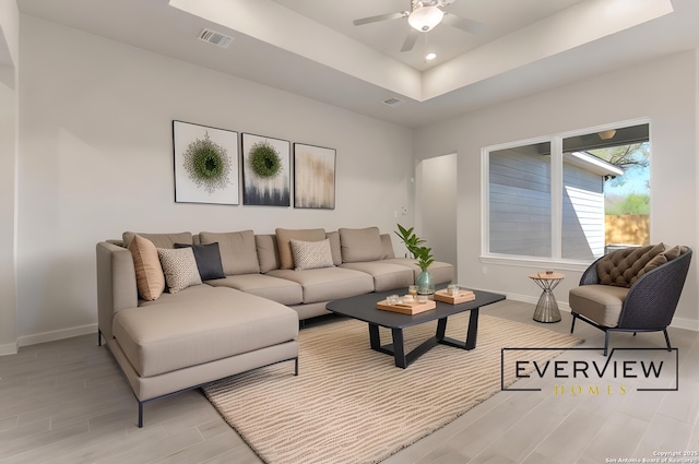 living room with a raised ceiling, ceiling fan, and light wood-type flooring