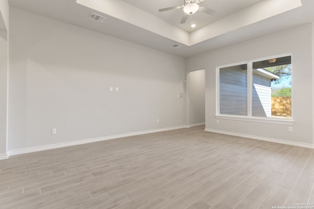 spare room featuring a tray ceiling, light hardwood / wood-style floors, and ceiling fan