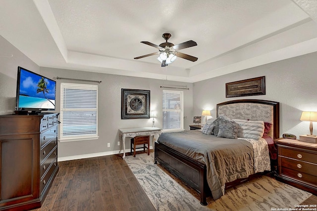 bedroom featuring ceiling fan, dark hardwood / wood-style flooring, a raised ceiling, and multiple windows