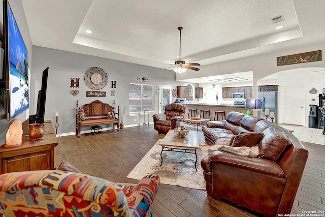 living room featuring hardwood / wood-style floors, a tray ceiling, and ceiling fan
