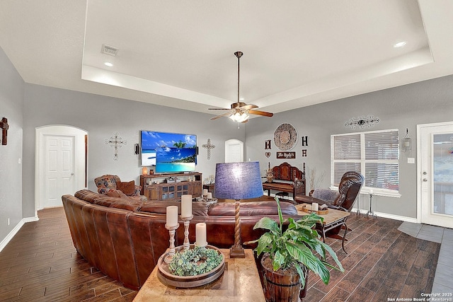 living room with dark hardwood / wood-style flooring, a tray ceiling, and ceiling fan