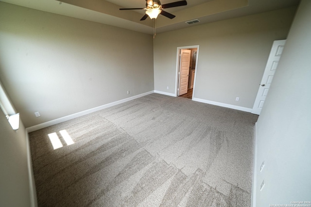 carpeted empty room with a raised ceiling and ceiling fan