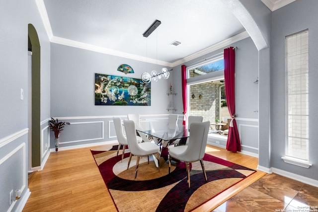 dining space with a wainscoted wall, arched walkways, a decorative wall, and crown molding