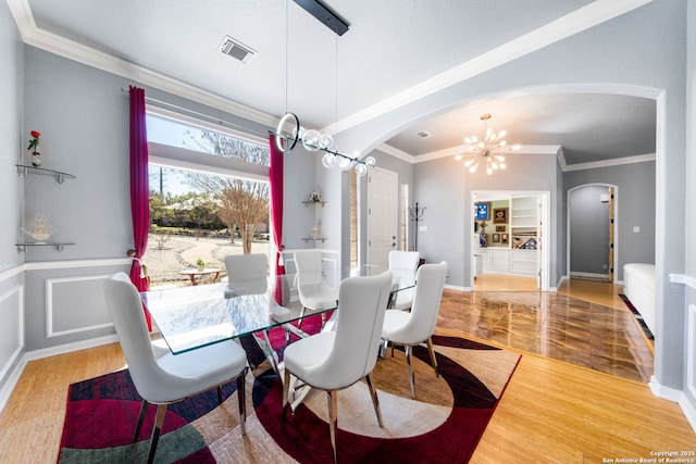 dining space featuring arched walkways, a wainscoted wall, visible vents, ornamental molding, and a chandelier