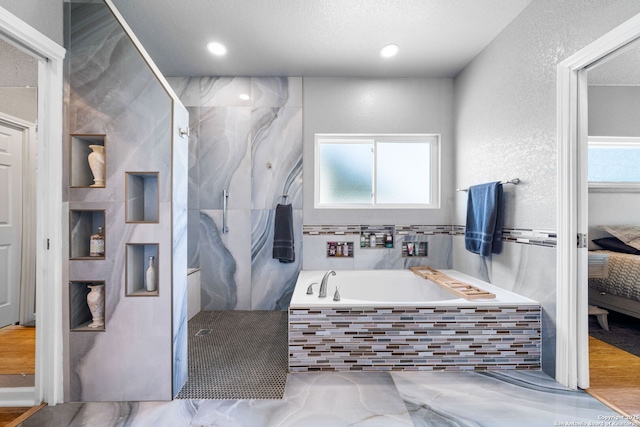 bathroom with ensuite bathroom, a textured wall, plenty of natural light, and a bath