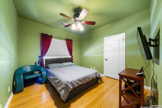 bedroom featuring visible vents, ceiling fan, baseboards, and wood finished floors