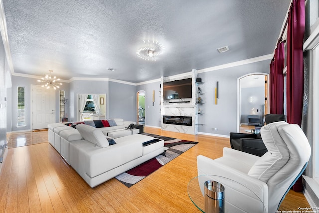 living room featuring light wood finished floors, visible vents, arched walkways, a premium fireplace, and a notable chandelier